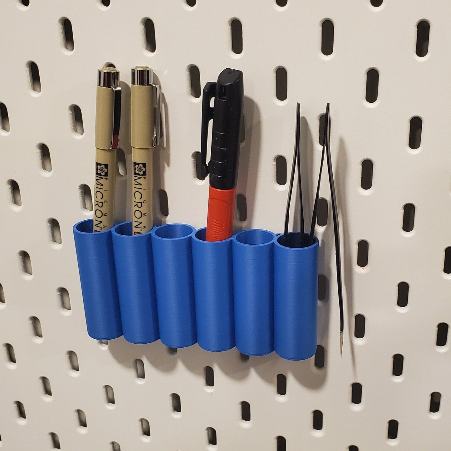 Blue Pegboard organizer with pens, sharpie, and tweezer storage.