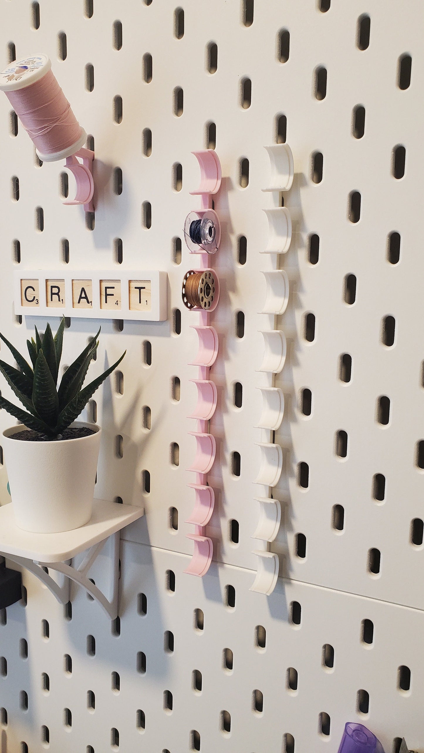 Two Bobbin Storage hooks next to an IKEA SKADIS Plant and a Craft Scrabble sign